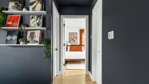 Ein Flur mit einer dunklen Wand, einer weißen Tür, die zu einem Schlafzimmer führt, und einem Regal mit Büchern und Pflanzen.