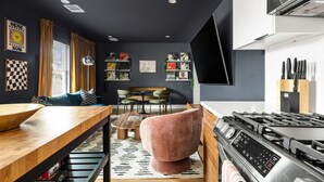 Eine moderne Küche mit Gasherd, ein Essbereich mit Holztisch und Stühlen sowie ein Wohnbereich mit Sofa und Couchtisch.