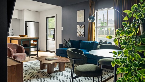 Ein modernes Wohnzimmer mit Sofa, Sesseln, Couchtisch, Esstisch und Küchenzeile mit Kühlschrank.