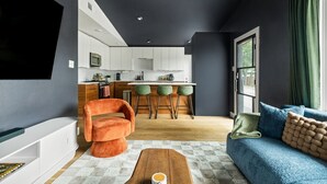 A modern living room with a sofa, a coffee table, and a vibrant orange chair. A kitchen with white cabinets and a bar area is visible in the background. - Wonderland Unit A · Sleeps 12, Hot Tub & BBQ (Austin)
