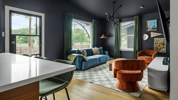 A modern living room with a sofa, chairs, a dining table, and a large window with curtains. - Wonderland Unit A · Sleeps 12, Hot Tub & BBQ (Austin)