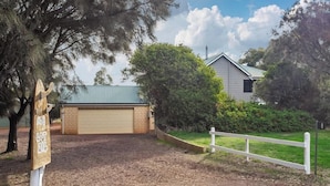 A residential property with a garage, a fenced yard, and a sign indicating a lot number. - Canopy House—Refined Bushland Haven near the Coast (Quedjinup)