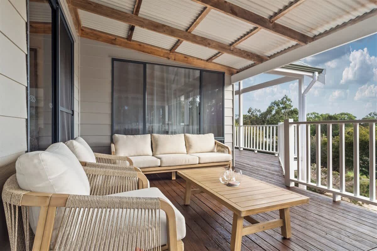 A covered outdoor seating area with a sofa and chairs, a wooden table, and a view of the surrounding landscape.