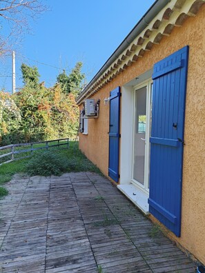 Un edificio con terraza de madera, una puerta azul y un ventanal con contraventanas.