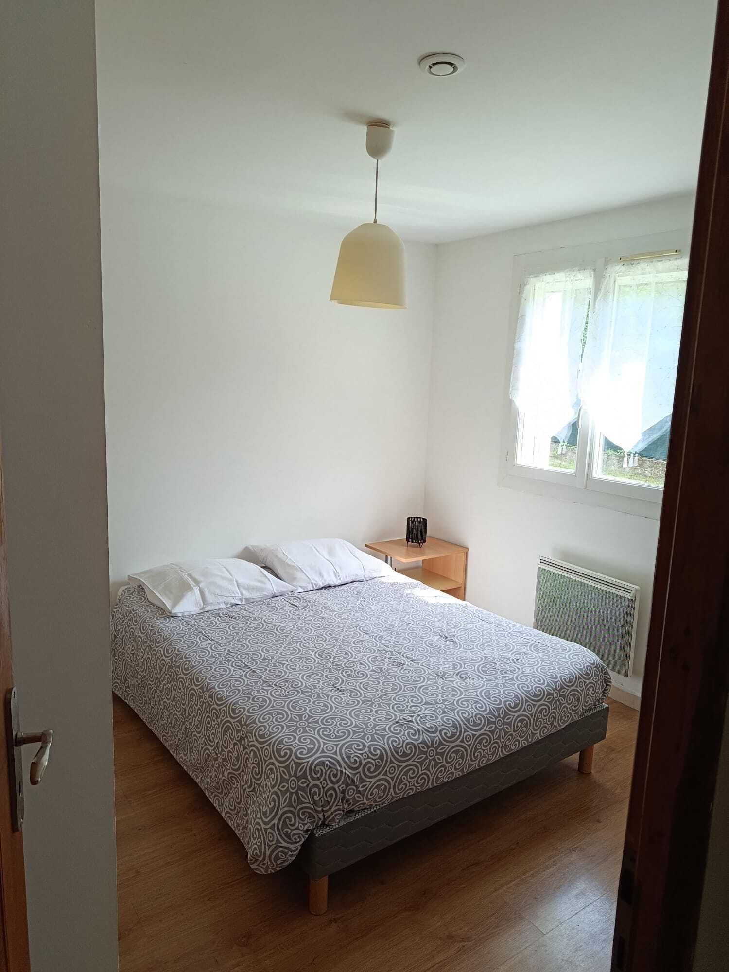 Un dormitorio con cama, mesita de noche, lámpara, radiador y ventana con cortinas.