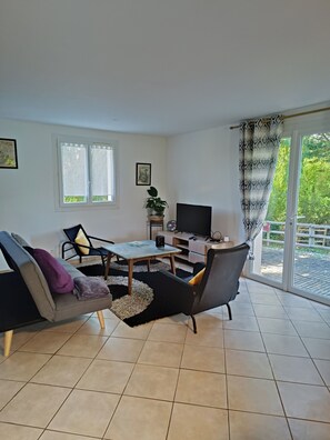 Sala de estar con sofá, mesa de centro, televisor y puerta corrediza al exterior.