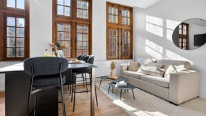A modern living room with a sofa, dining table, chairs, and a TV mounted on the wall. - Maison Grand-Place 2 (Brussels)