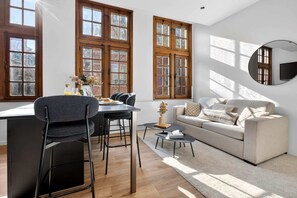 A modern living room with a sofa, dining table, chairs, and a TV mounted on the wall. - Maison Grand-Place 2 (Brussels)