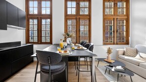 A modern kitchen with dark cabinetry, a dining table set for breakfast, and large windows with a view. - Maison Grand-Place 2 (Brussels)