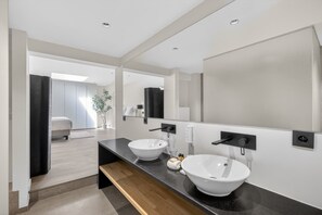Ein modernes Badezimmer mit zwei weißen Waschbecken, einem großen Spiegel und einer Holzbank.