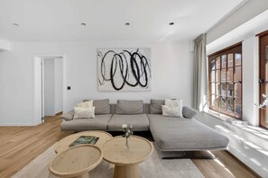 Ein modernes Wohnzimmer mit einem grauen Ecksofa, zwei runden Holztischen und einem großen abstrakten Gemälde an der Wand.