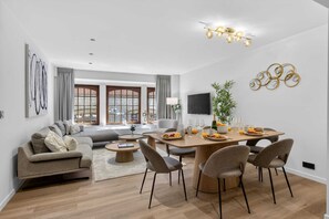 Ein modernes Wohnzimmer mit einer Couch, einem Couchtisch, einem Esstisch mit Stühlen und einem an der Wand befestigten Fernseher.