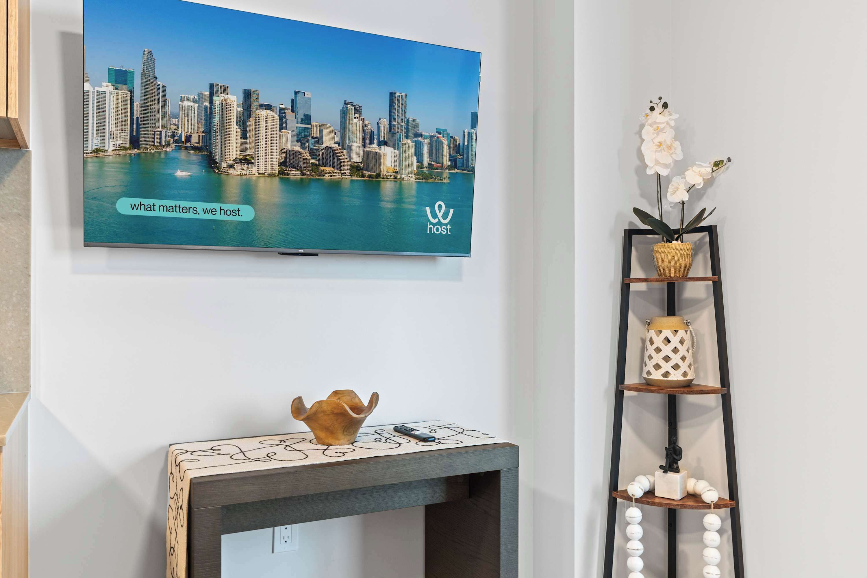 Un televisor montado en una pared muestra un paisaje urbano con el texto 'what matters, we host'.