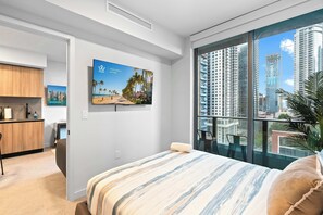 Ein modernes Hotelzimmer mit einem großen Bett, Blick auf die Stadt, einer Küchenzeile und einem Essbereich.