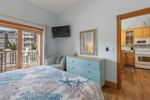 Een slaapkamer met een bed, een televisie, een dressoir en een keukenhoek met kasten en apparatuur.