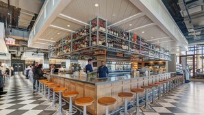 Een bar met krukken, een hoge plafond en planken vol flessen.