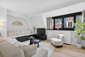 Ein modernes Wohnzimmer mit einer Couch, Sesseln, einem Couchtisch und einem Fernseher.