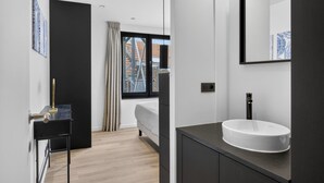 A modern bathroom with a large window, a white sink, and a dark vanity.
