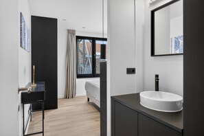 Ein modernes Badezimmer mit großem Fenster, einem weißen Waschbecken und einem dunklen Waschtisch.
