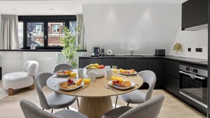 A modern kitchen with a dining table set for breakfast, a window with curtains, and a view of buildings outside.