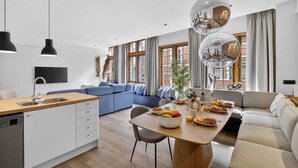 Une cuisine moderne dotée d’un plan de travail en bois et d’un lave-vaisselle encastré, un coin repas avec une table ronde et des chaises, et un salon avec un canapé et une grande fenêtre.