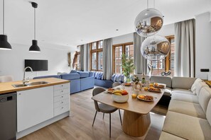 A modern kitchen with a wooden countertop and a built-in dishwasher, a dining area with a round table and chairs, and a living room with a sofa and a large window. - Maison Grand-Place C (Brussels)