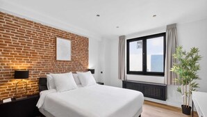 Une chambre d’hôtel moderne avec un mur d’accent en briques, un grand lit, une fenêtre donnant sur un beau paysage et une plante en pot.