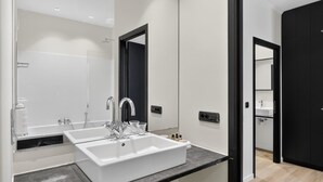 Une salle de bain moderne avec un lavabo blanc, deux robinets, un miroir et une douche.