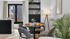 Un comedor moderno con una mesa redonda, sillas tapizadas en gris, una consola negra y una lámpara de pie.