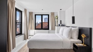Habitación de hotel moderna con una cama grande, una mesita de noche, una ventana con cortinas y vistas a la ciudad.