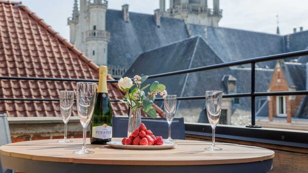 Una mesa con una botella de vino Pugetisser, un plato de fresas y copas de vino vacías en un balcón con vistas a un castillo.