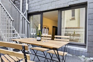 Ein Holztisch mit vier Stühlen, einer Champagnerflasche und zwei Gläsern auf einem Balkon mit Blick ins Innere des Gebäudes.