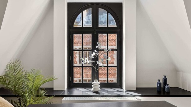 Un intérieur moderne avec une fenêtre à cadre noir, un vase blanc et une plante.