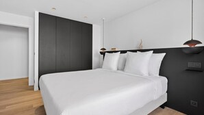 Une chambre moderne avec un grand lit, une tête de lit sombre et un luminaire suspendu.