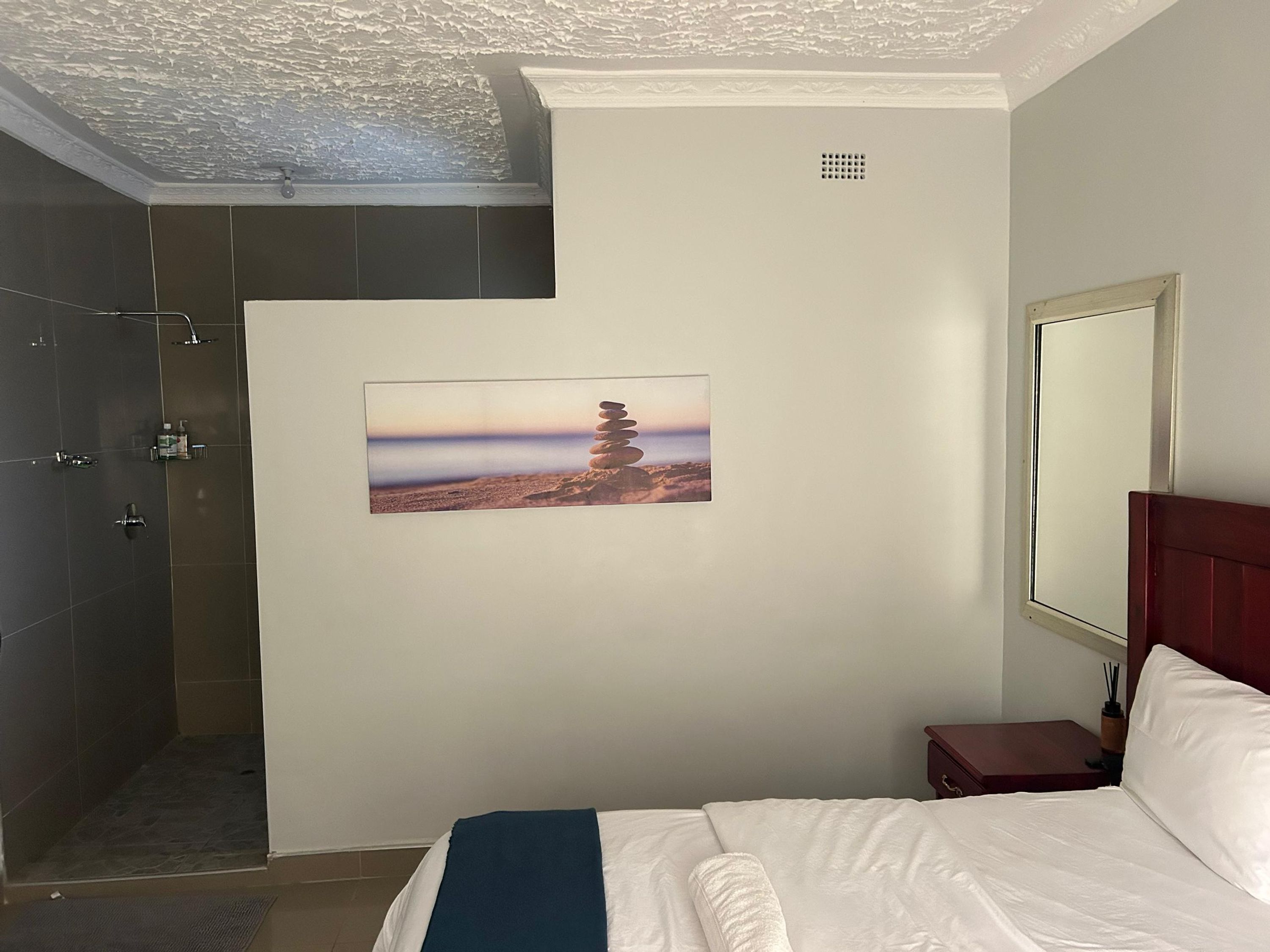 A hotel room with a bed, a shower, a picture of a tree on the wall, and a window.