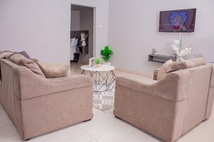 Una sala de estar con dos sofás color beige, una mesita blanca con una planta y un televisor en la pared.