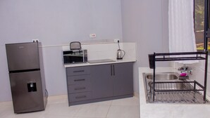 A compact kitchen with a refrigerator, microwave, sink, and a dish rack.