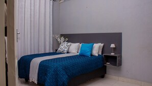 A bedroom with a bed, a nightstand, a lamp, and a wall-mounted air conditioner.