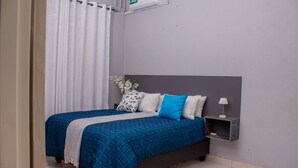 A bedroom with a bed, a nightstand, a lamp, and a wall-mounted air conditioner.