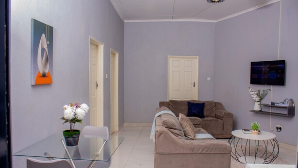 A living room with a sofa, a glass table, a TV, and a door.