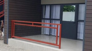 A modern building with a covered entrance, a red railing, and a staircase leading up to a balcony. - One Bedroom Modern Apartment in Fomona - 2386 (Bulawayo)