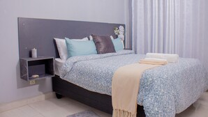 Quarto com cama, almofadas, mesa de cabeceira e janela com cortinas.