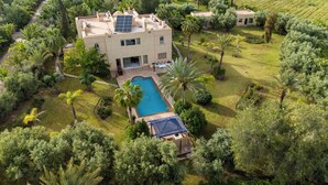 A large building with a swimming pool, surrounded by lush greenery and palm trees. - Villa Aurea (Marrakech)
