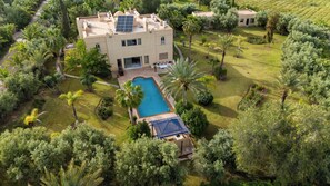 Un edificio grande con piscina, rodeado de abundante vegetación y palmeras.