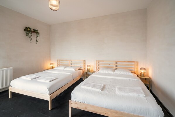 Two wooden beds with white linens and towels, bedside lamps, and a wall-mounted plant. - 2BR City Stay - Grand Central Area (Antwerp)