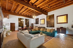 A spacious living room with a high wooden ceiling, a green sofa set, a white sofa, and a dining area with a table and chairs. - 'Grimilda' Apartment with Shared Pool, Wi-Fi and Air Conditioning (Piombino Dese)