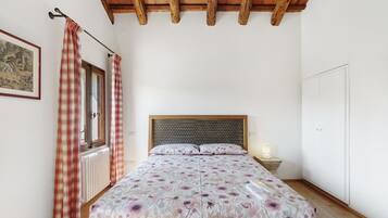 Une chambre à coucher avec un lit, une fenêtre avec des rideaux, un radiateur, un plafond en bois et une porte.