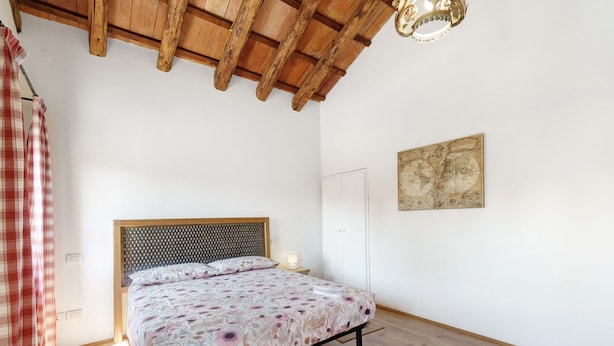 Un dormitorio con techo de madera, una cama con ropa de cama floral, un globo de pared y una cortina escocesa.