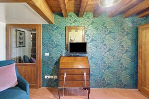 Ein Zimmer mit Holzbalkendecke, einem Fernseher auf einer Holzkommode und einem gemusterten Wandpapier.
