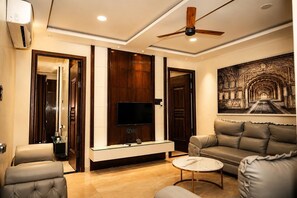 A modern living room with a flat-screen TV, leather sofas, a ceiling fan, and a decorative wall mural.